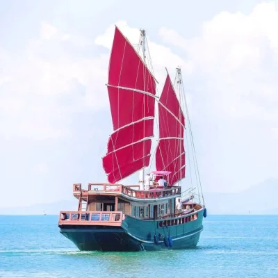 Traditional wooden junk sailboat with iconic red sails cruising on clear blue sea for Angthong National Marine Park day cruise tour